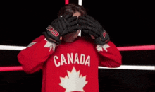 a young man wearing a red canada jersey and gloves is standing in front of a camera .
