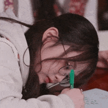 a girl wearing glasses is writing on a piece of paper with a green marker that says kc on it