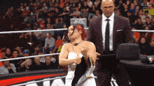 a woman in a white dress stands in a wrestling ring next to a man in a suit and tie