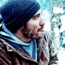 a man wearing a hat and a jacket is smoking a cigarette in the snow .
