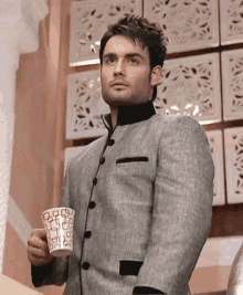 a man in a suit is holding a cup that has a pattern of squares on it