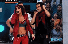 a woman in a red jacket sings into a microphone while a man holds a microphone