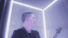 a man is playing a guitar in a purple room with a purple light behind him .