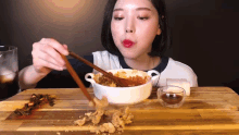 a woman is eating a bowl of food with chopsticks ..