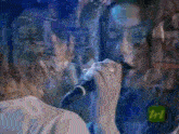 a woman singing into a microphone with a tri logo on the bottom left