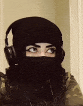 a woman wearing a beanie and headphones has a black face mask on