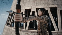 a woman is holding a bow and arrow in front of a building with the letter w on the bottom