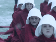 a group of women in red robes and white hats are kneeling down