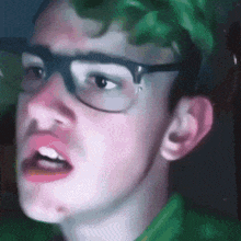 a young man wearing glasses and a green shirt is making a funny face