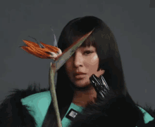 a woman in a fur coat is holding a flower in front of her face