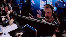 a man wearing headphones is sitting in front of a computer monitor with a red bull cooler in the back