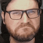 a close up of a man with glasses and a beard making a face .
