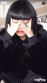 a woman in a fur coat covering her face with her hands and a ring in her finger
