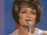 a woman singing into a microphone with a purple background