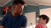 a man and a boy are standing in a room with a poster on the wall that says " slow much "