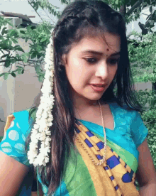 a woman wearing a blue yellow and green saree with flowers in her hair