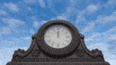 a clock with roman numerals and a blue sky in the background shows the time as 11:55