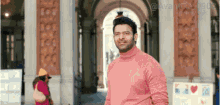 a man wearing a pink turtleneck is standing in front of a building