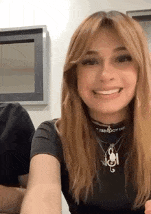 a woman wearing a black t-shirt and necklaces is smiling and looking at the camera .