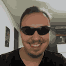 a man wearing sunglasses and a black shirt is smiling and looking at the camera .