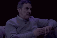 a man wearing a grey sweater has a badge on his neck that says ' lg ' on it