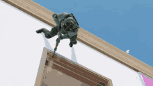 a man in a green uniform is holding a gun while climbing up a wall