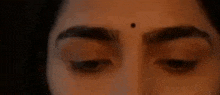 a close up of a woman 's eyes with a small black spot on her forehead .