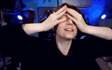 a person covering their eyes with their hands while smiling
