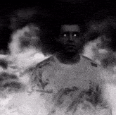 a man in a white shirt with arabic writing on it stands in front of smoke