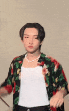 a young man wearing a floral shirt and a pearl necklace is holding a drum stick .