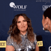 a woman in a sequined dress is talking to another woman in front of a wall that says wolf entertainment