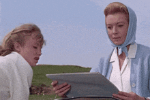 a woman wearing a head scarf looks at a tablet while another woman looks on