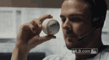 a man wearing a headset is holding a baseball in his hand in front of mlb.com