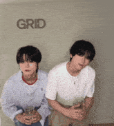 two young men are sitting in front of a wall that says grid