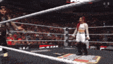 a female wrestler stands in the middle of a wrestling ring with a crowd behind her