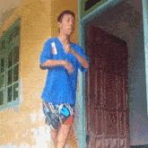 a young man in a blue shirt and shorts stands in front of a door