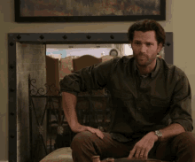 a man in a green shirt sits in front of a fireplace with a painting on the wall
