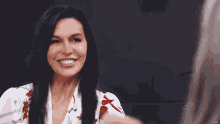 a woman in a white shirt with red flowers smiles