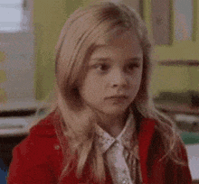a young girl in a red jacket is sitting in a classroom .