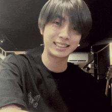 a young man wearing a black t-shirt with a butterfly on it smiles for the camera .