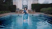 a woman in a blue dress is sitting in a chair in a pool reading a book