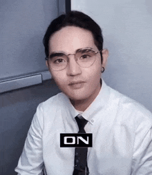 a man wearing glasses and a white shirt and tie is sitting in a room .