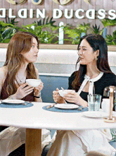 two women sit at a table in front of a sign that says duchess