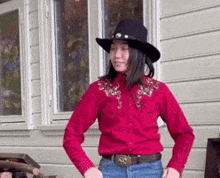 a woman wearing a cowboy hat and a red shirt is standing in front of a house