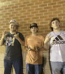 three young men are posing for a picture and one has an adidas shirt on
