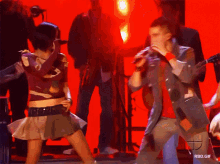 a man singing into a microphone while a woman dances in front of a red background with rbd.gif written on it