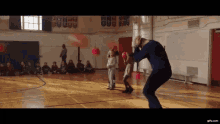 a group of children are sitting on the floor in a gym watching a man boxing a child