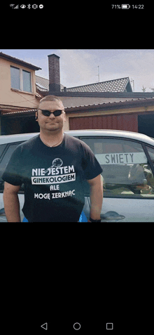 a man wearing a shirt that says nie jestem ginekologiem stands in front of a white car