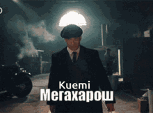 a man in a suit and tie is standing in a dark room with the name kuemi megaxapov on the bottom
