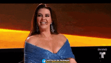a woman in a blue dress is smiling while sitting in front of a microphone .